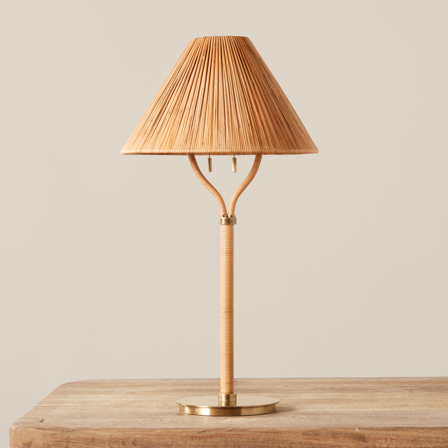 A rattan table lamp in a warm natural tan color, on a wooden table, against a plain light beige background.- Number 1