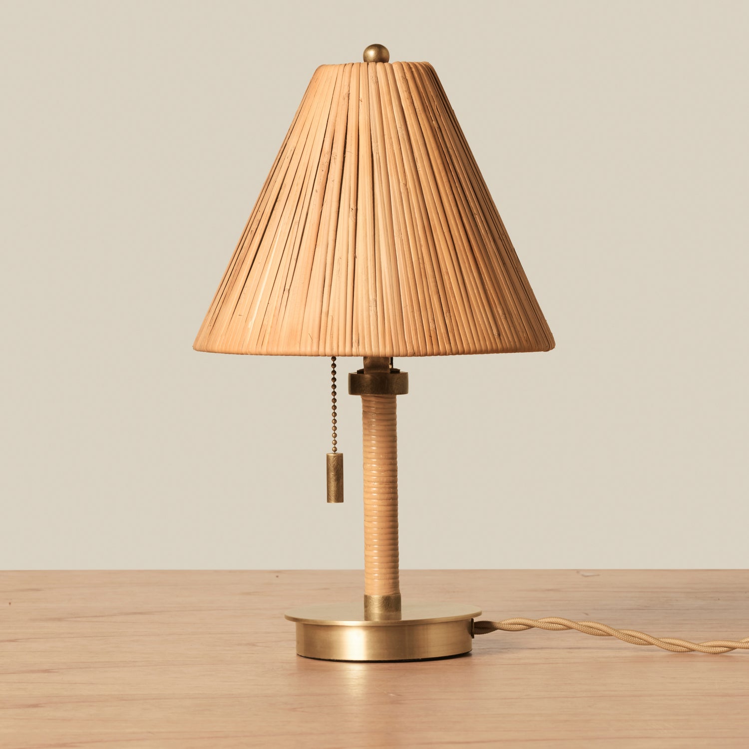 Small rattan table lamp with brass accents on wooden table against beige background- Number 1