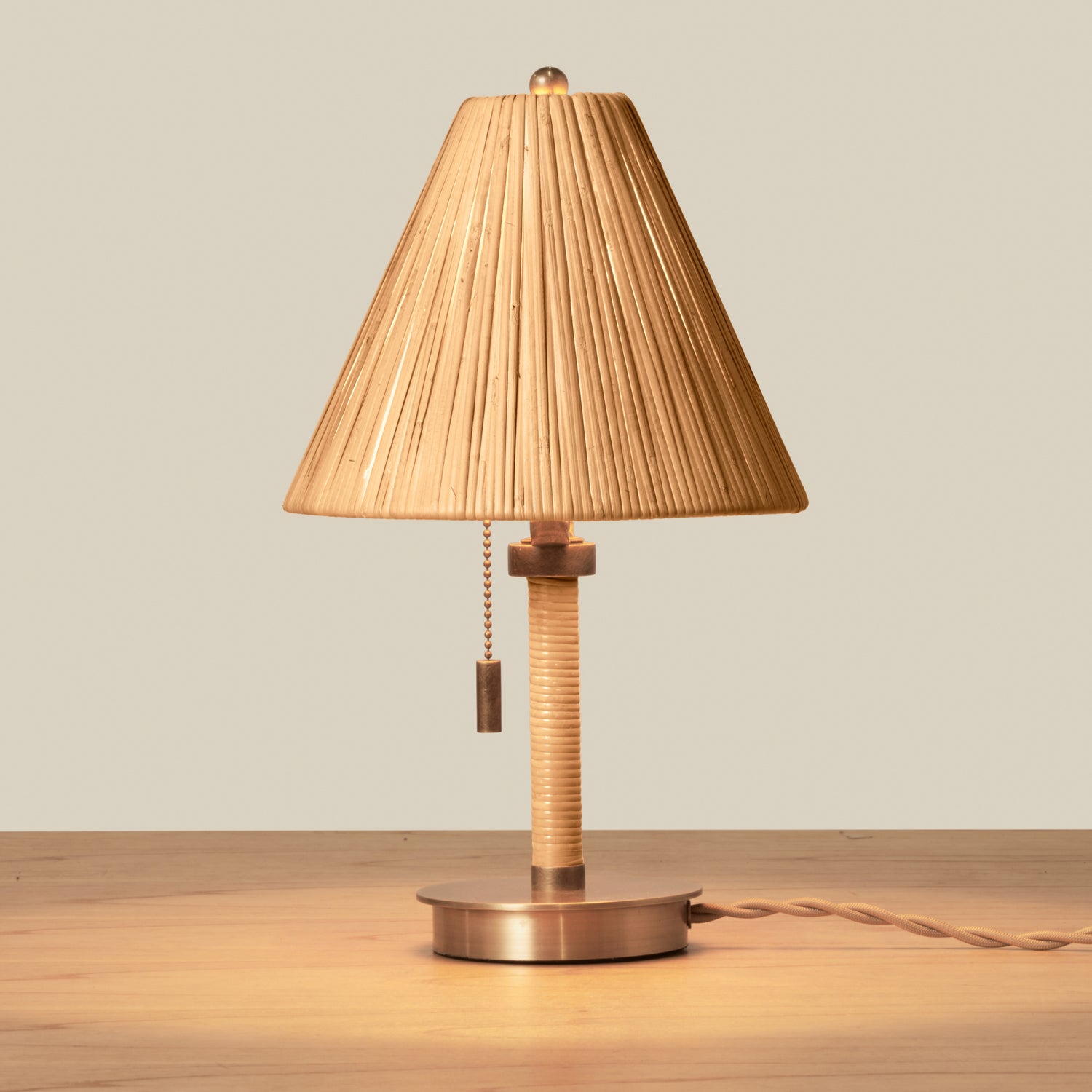 Small rattan table lamp with brass accents on wooden table against beige background- Number 4