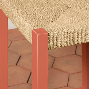 Close-up of a woven chair seat with a red frame on a brick patio. - Number 6
