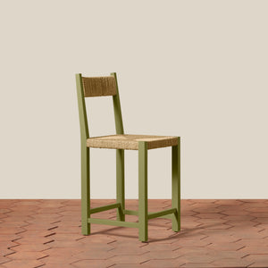 Green bar stool with woven seat on a wooden floor and beige wall background - Number 19