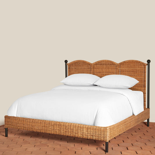 Bed with wicker headboard and footboard on a wooden floor against a beige wall