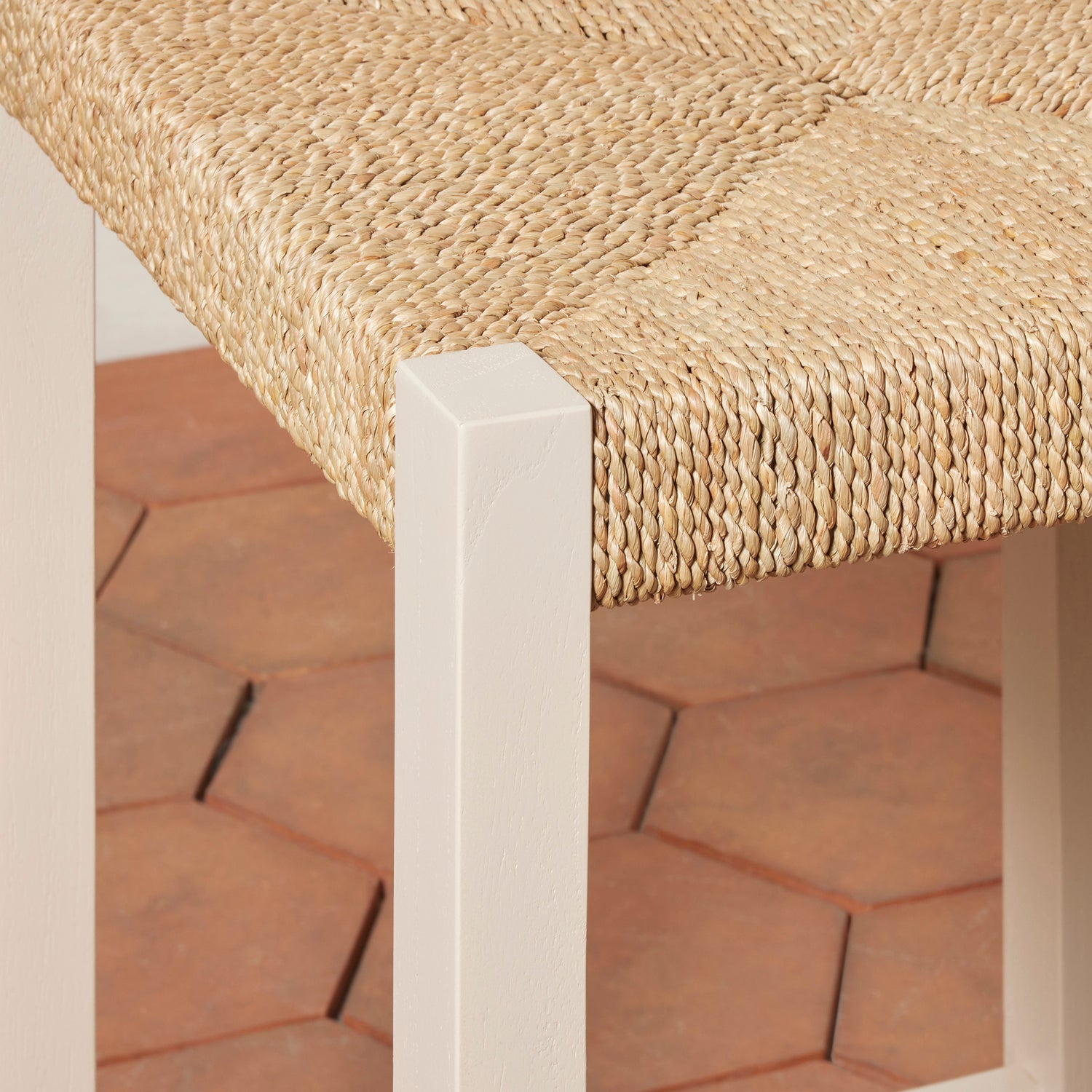 Close-up of a woven seat with a white frame on a brick floor.- Number 18