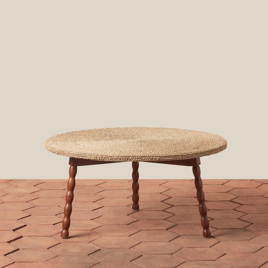 Round woven table with wooden legs on a wooden floor.