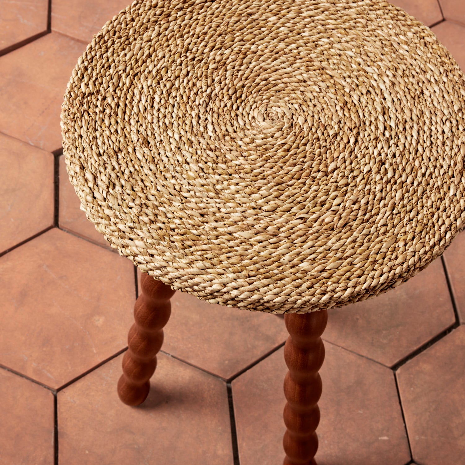 Round woven stool with wooden legs on a hexagonal tiled floor- Number 4