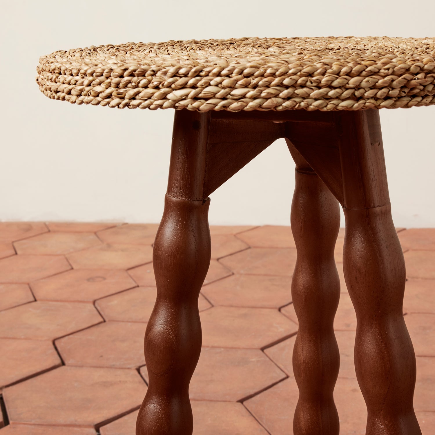 Round woven table with twisted wooden legs on a terracotta floor.- Number 5