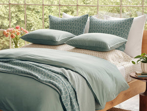 Bed with green bedding and pillows in a bright room with flowers and plants. - Number 3