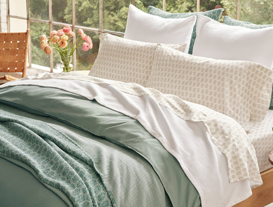 Bed with green and white bedding, pillows, and a vase of flowers on a wooden chair. - Image 2