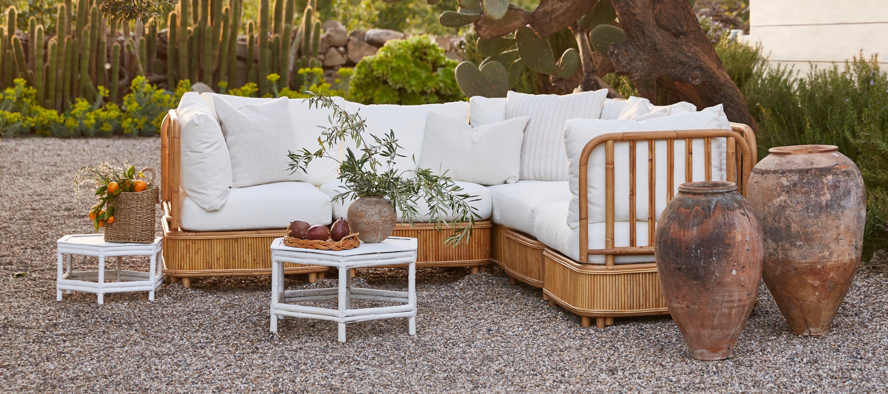 Outdoor patio with wicker sectional sofa, small tables, and decorative pots in a garden setting.