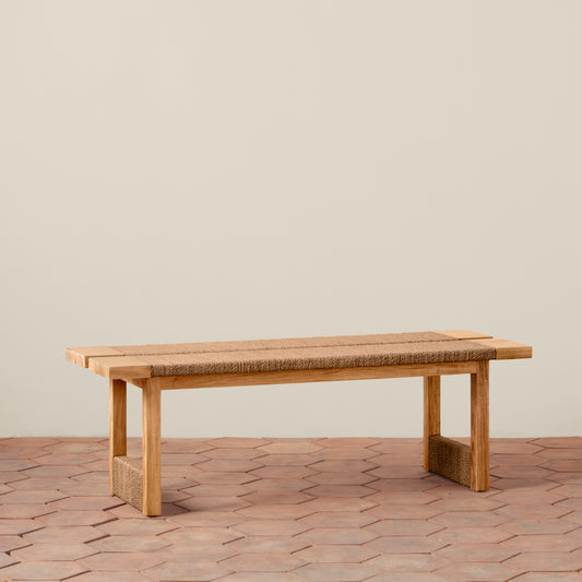 Wooden bench with woven seat on a wooden floor against a beige wall