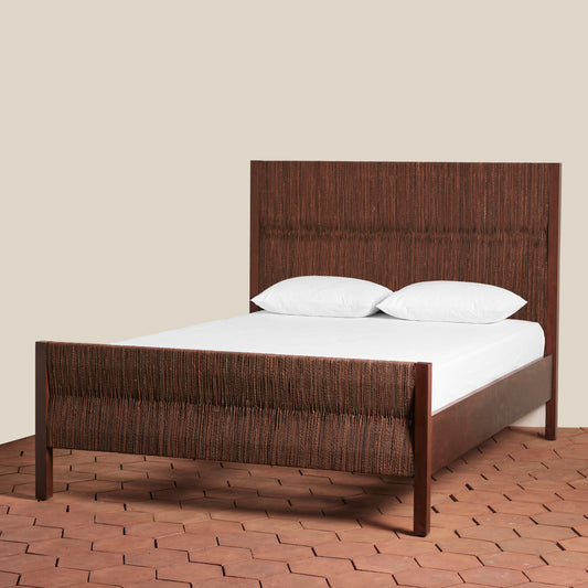 Dark wood framed bed with woven seagrass headboard and footboard with white bedding on a beige background.