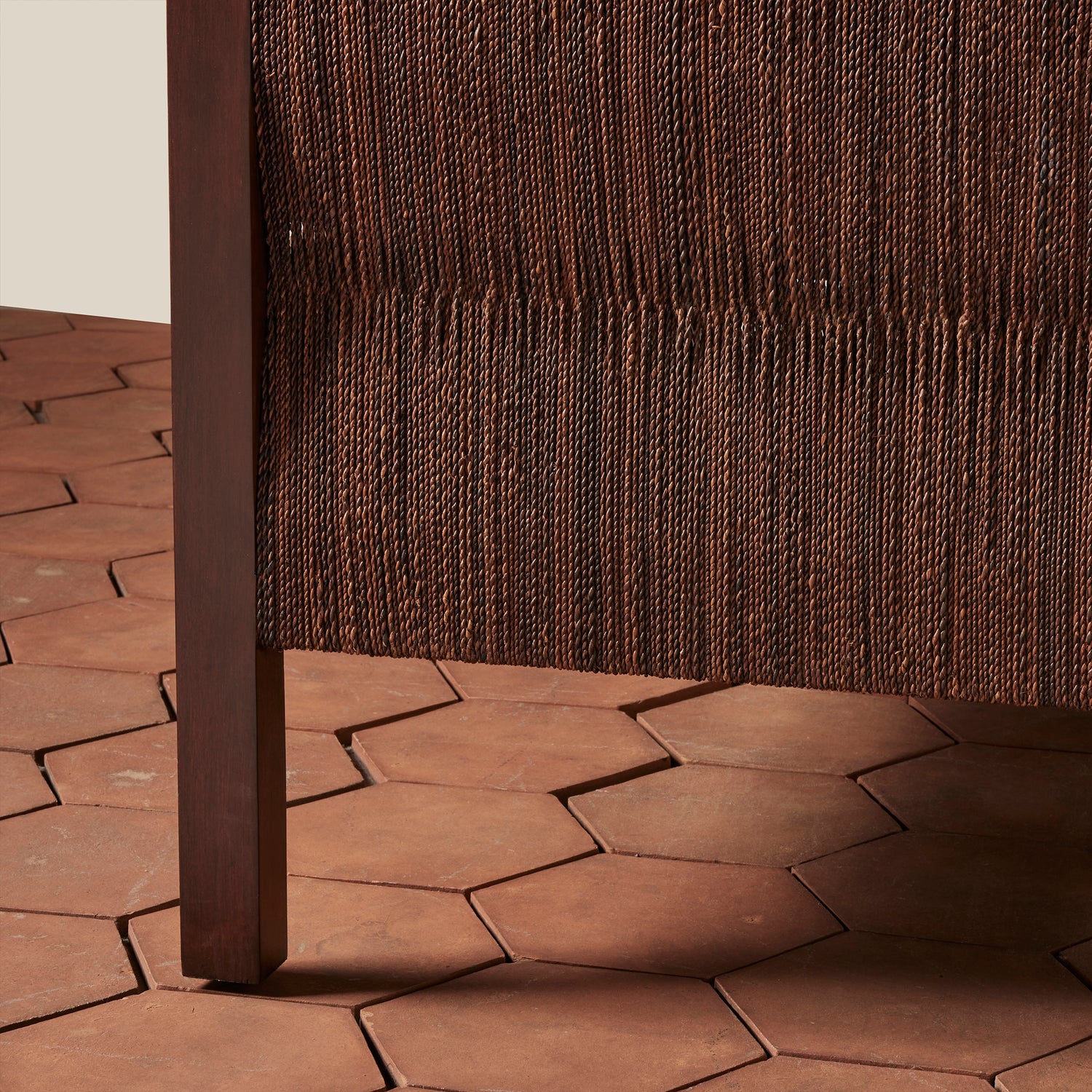 Brown woven chair with a textured wall and hexagonal brown tiles on the floor.- Number 10