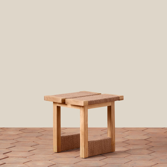 Wooden stool with woven seat and backrest on a wooden floor.