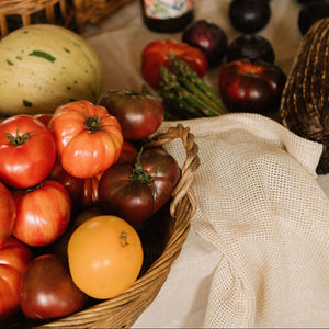 A rustic table arrangement featuring a wicker basket filled with assorted heirloom tomatoes, including red, orange, and dark purple varieties, alongside other fresh vegetables and wicker baskets in a warm, cozy setting. - Number 2