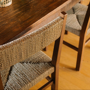 A close-up of a wooden dining table with woven-back chairs, styled with tomatoes, glasses, and a bottle in a warm indoor setting. - Number 3