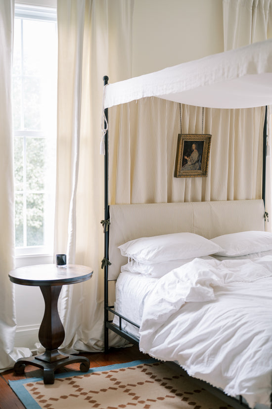 Bedroom with a canopy bed, white bedding, and a side table.