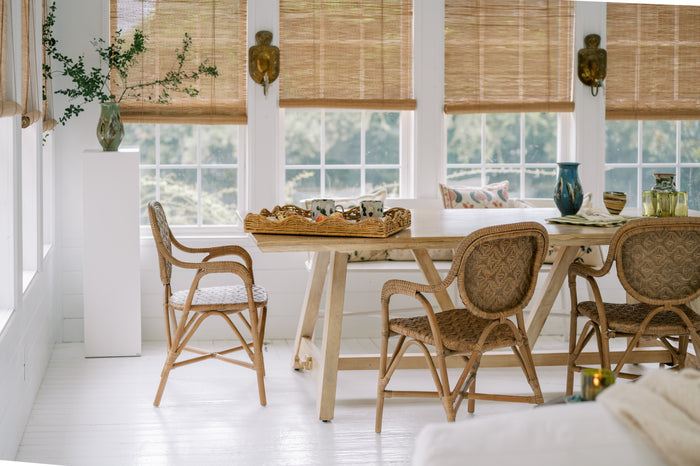 Dining area with wooden table and chairs in a bright room with large windows.