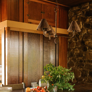 A rustic dining room scene featuring a dark wood dining table with woven-back chairs, a hanging multi-light chandelier, a stone wall, and a potted green plant on the table. - Number 2